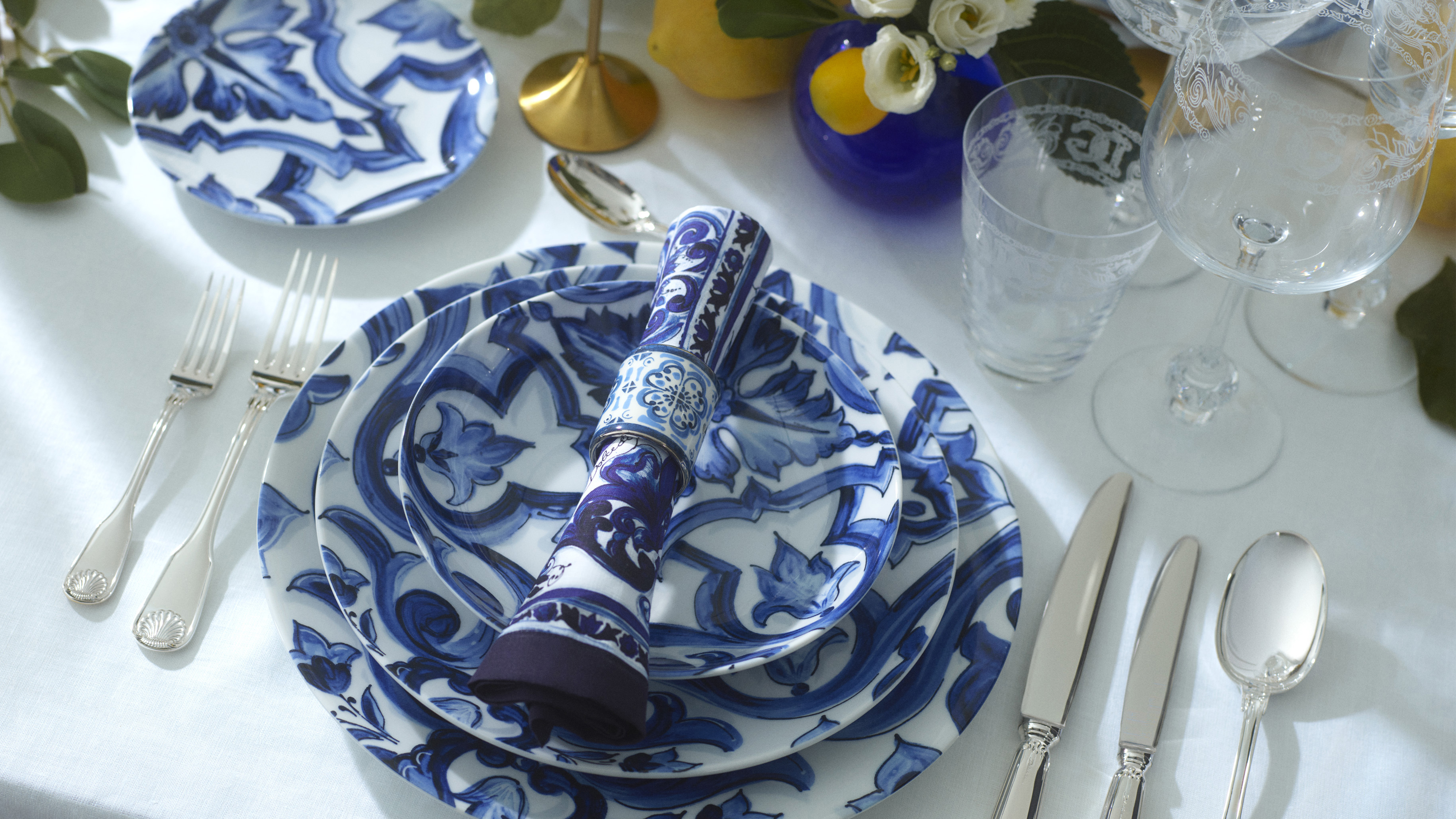Nakrycie Blu Mediterraneo z góry — talerze, serwetka, sztućce i kryształy
